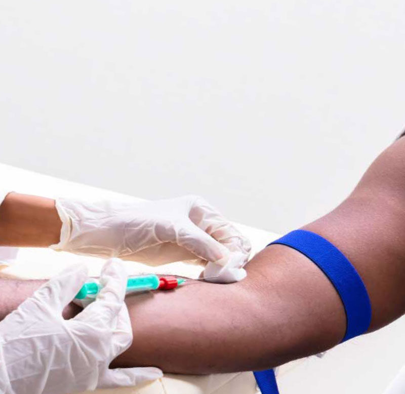 Young dark skin tone man in grey shirt having blood drawn by healthcare worker in medical gloves.